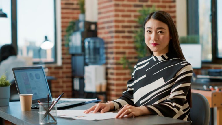 Image of a South Korean entrepreneur working behind her desk and smiling in the direction of the camera.